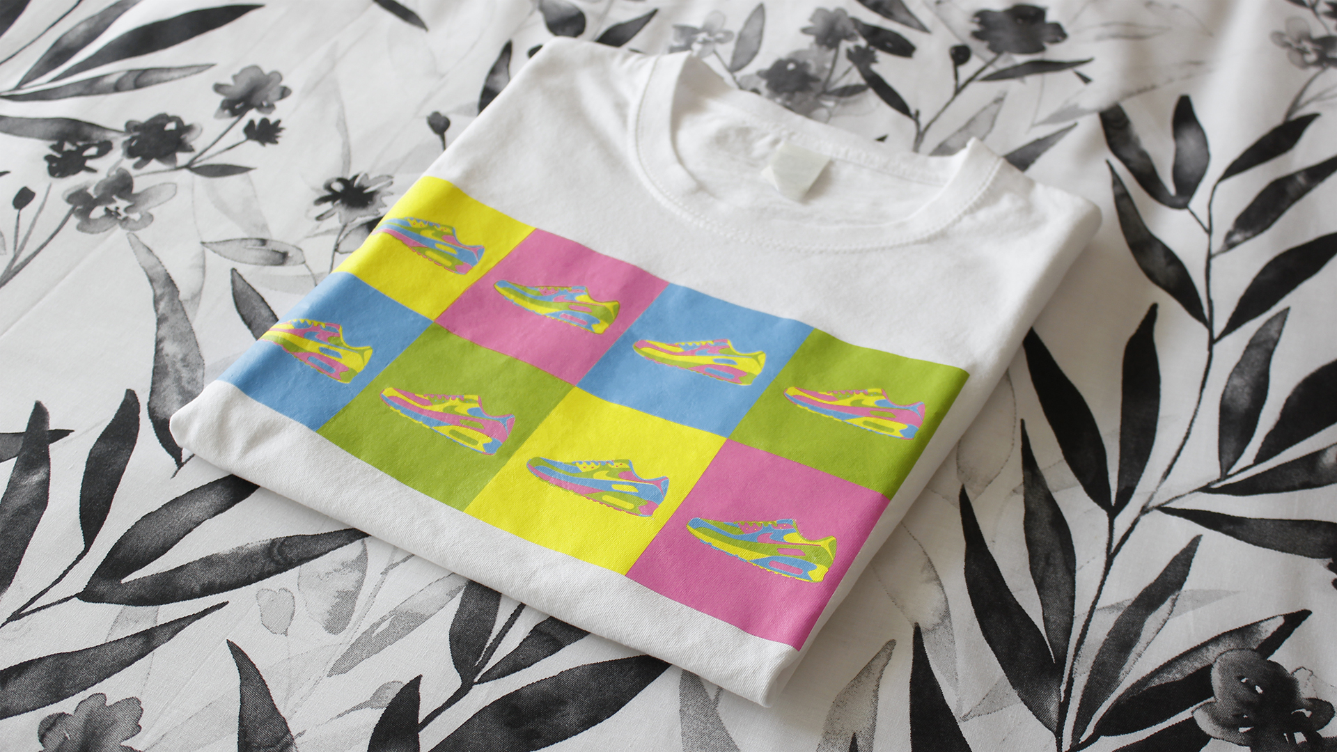 Fotografía real de una camiseta blanca doblada que lleva impresa la ilustración conjunta de 'Air Max 90 Warhol Style'